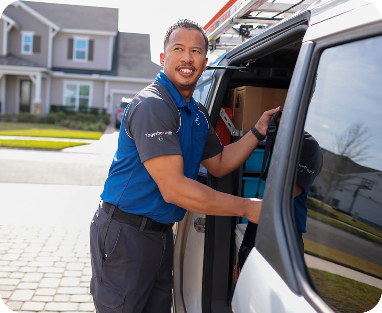 A technician in an ADT uniform smiles while unloading equipment from a service van parked in a suburban neighborhood.