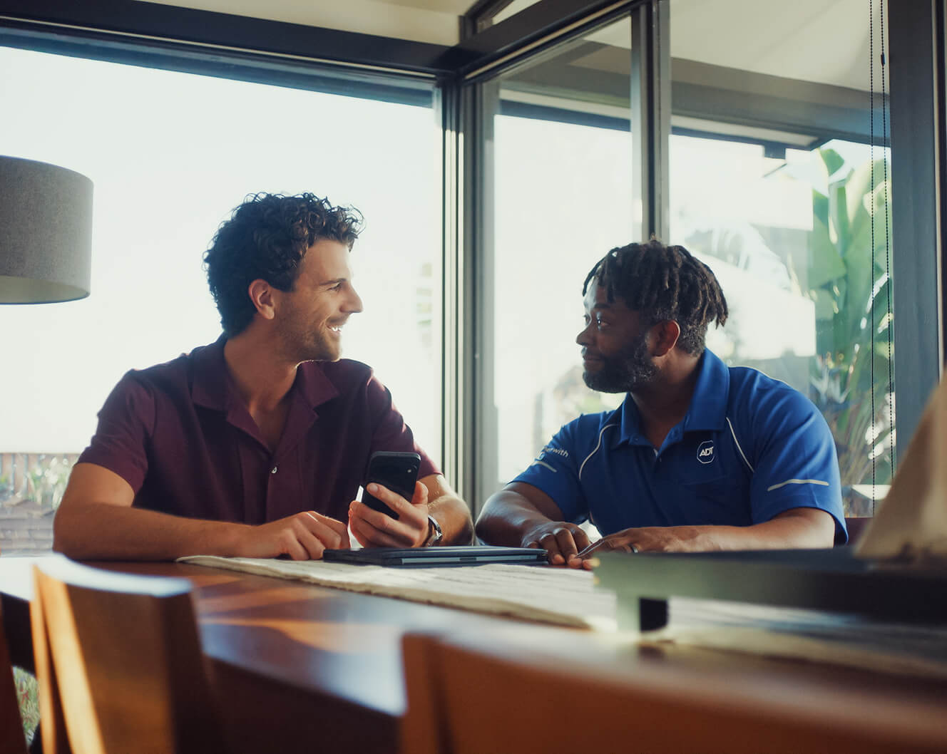 An ADT professional sits at a table with a homeowner, professional installation information together on a mobile device.