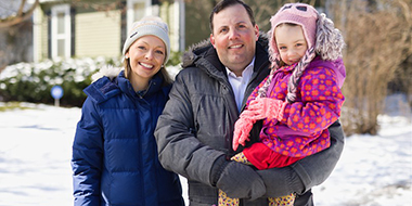 Image of three family members outside their home on a snowy day 